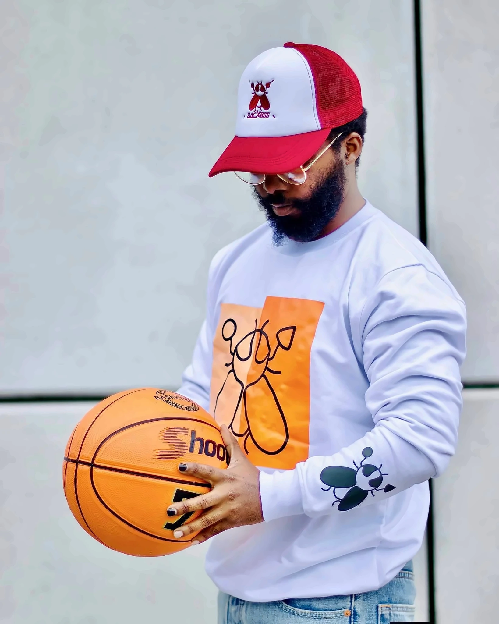 A man in a SACXESS trucker cap and long-sleeve beetle-print top holding a basketball